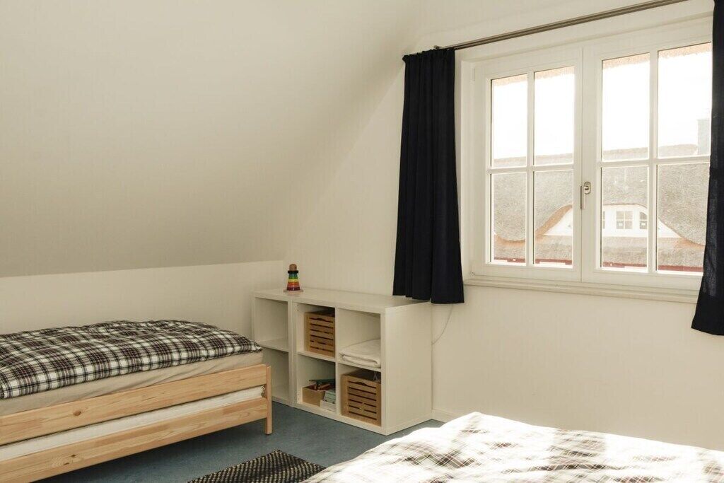 Een slaapkamer met een enkel bed, een raam met gordijnen en inbouwopbergruimte.