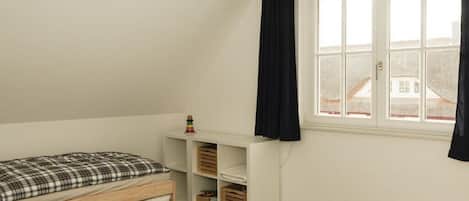 Een slaapkamer met een enkel bed, een raam met gordijnen en inbouwopbergruimte.
