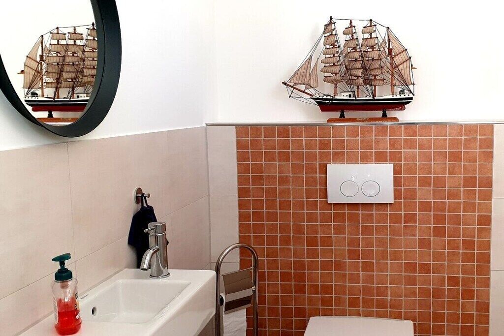 Casa de banho com lavatório, espelho e modelo de navio decorativo.