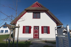 A two-story house with a steeply pitched roof, a red door, and red shutters. - Thatched House "H.A.L.O" (Zierow)