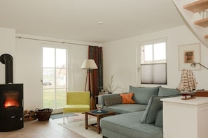 A living room with a fireplace, a sofa, a chair, and a table. - Thatched House "H.A.L.O" (Zierow)
