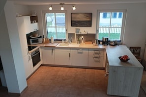 A kitchen with a central island, white cabinetry, a microwave, and a sink. - Thatched House "H.A.L.O" (Zierow)