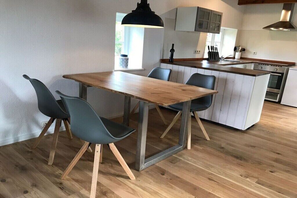 A modern kitchen with a wooden table and chairs, a built-in island, and a window providing natural light.