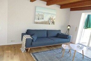 A living room with a blue sofa, a patterned rug, a painting of a beach, and a lamp. - Fischerkate Norderfeld (Dollerup)