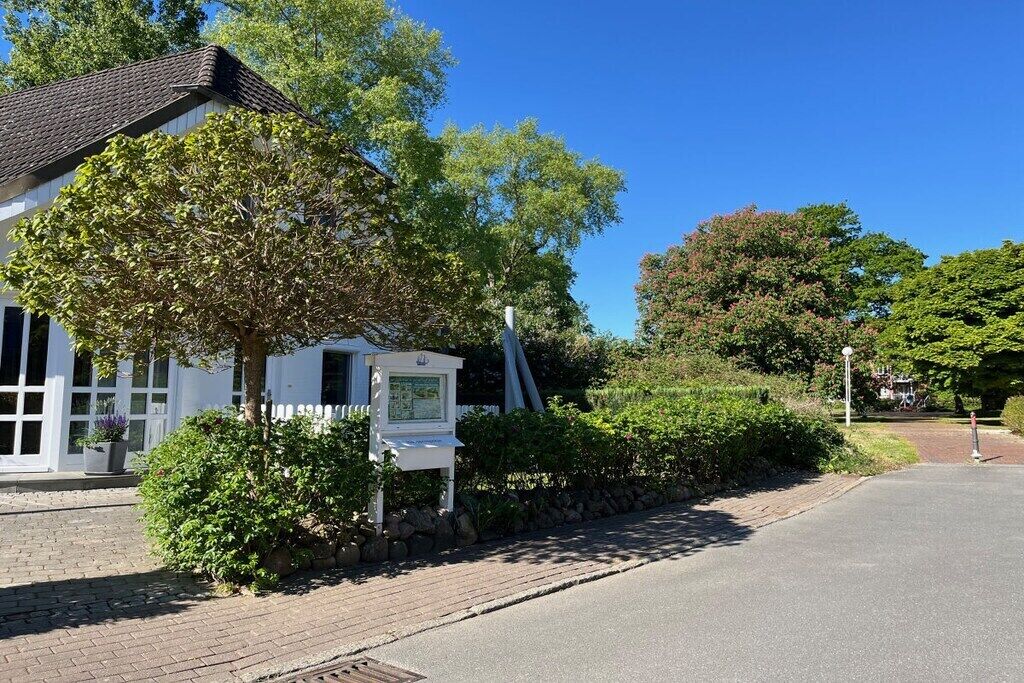 A white building with a tiled roof, a paved driveway, and a signboard.