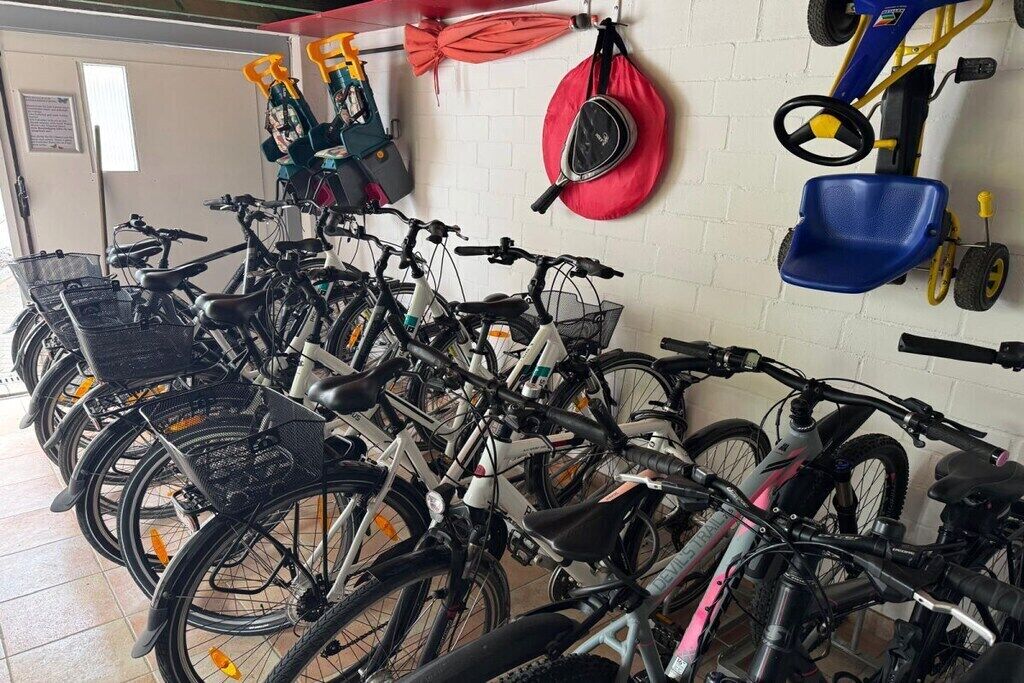 Varias bicicletas estacionadas en el interior, con un paraguas rojo y una cortadora de césped en la pared.