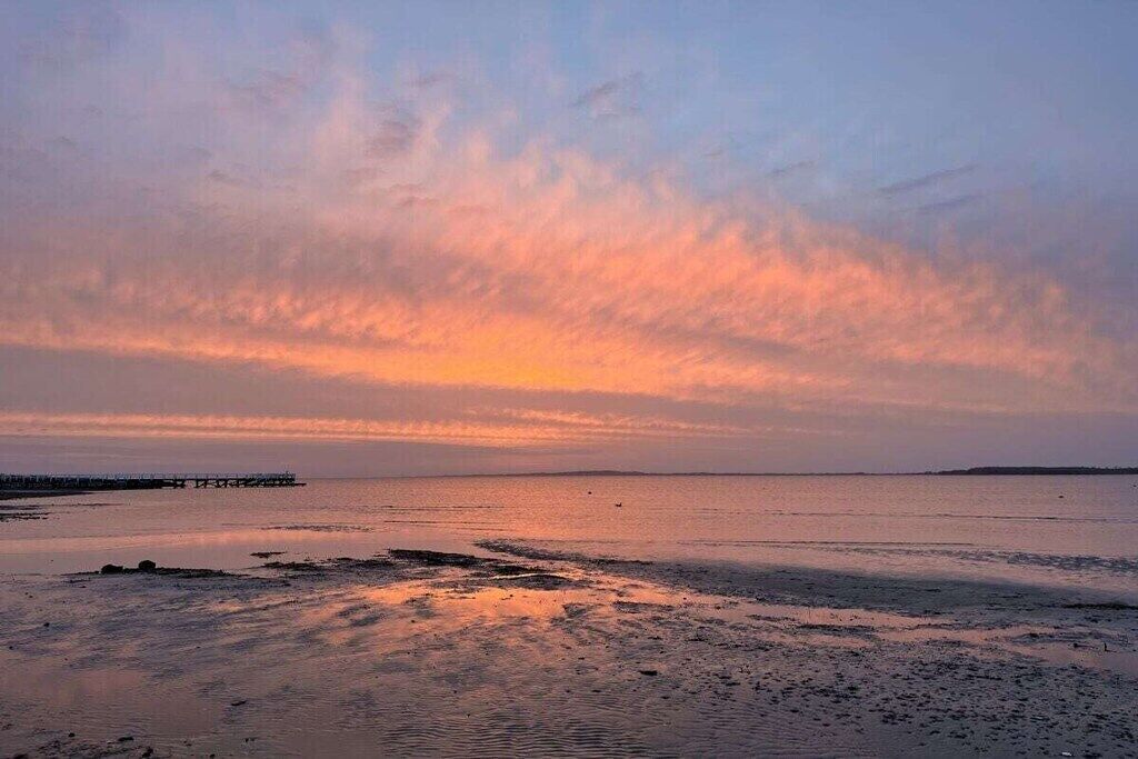 A beach with a pier extending into calm waters during sunset.