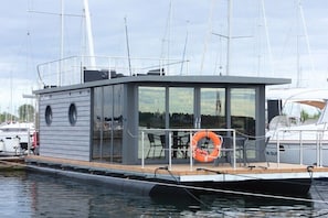A modern boat with a covered deck, a lifebuoy, and a view of the marina. - Houseboat in Wendtort with swimming pool (Wendtorf)
