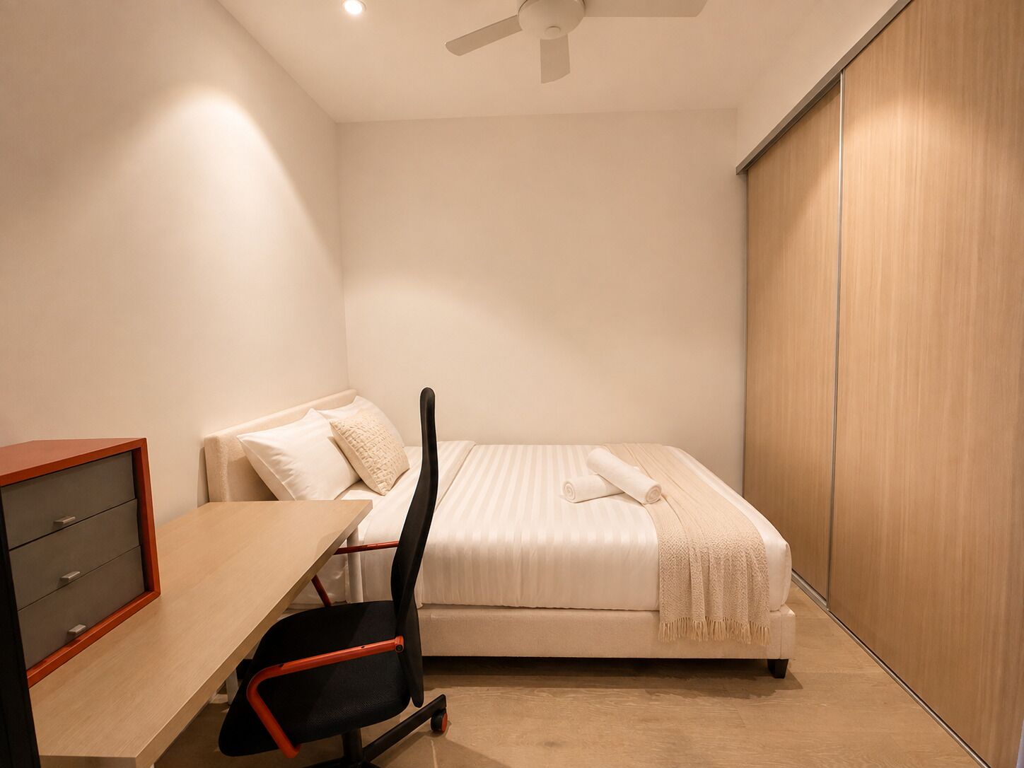 A bedroom with a bed, a desk with drawers, a chair, and a wardrobe.