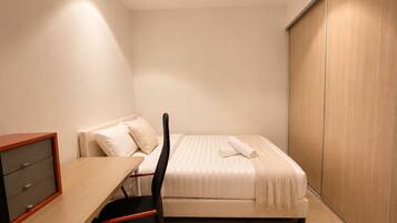 A bedroom with a bed, a desk with drawers, a chair, and a wardrobe.