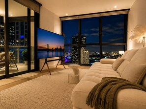 A modern living room with a large TV, comfortable seating, and a city view. - Elevated Elegance - Scenic Views in level 17 w/parking (Brisbane City)