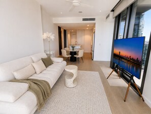 A modern living room with a sofa, coffee table, and a painting on a stand. - Elevated Elegance - Scenic Views in level 17 w/parking (Brisbane City)