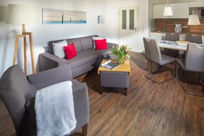 Een moderne woonkamer met een bank, een voetenbankje en een eethoek met stoelen en een tafel.