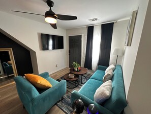 A modern living room with teal sofas, a coffee table, a ceiling fan, and a flat-screen TV. - Summerhill ATL Gem Walk to Stadium, Bars & Dining (Atlanta)