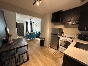 A modern kitchen with a refrigerator, stove, and microwave. There is a dining area with a table and chairs. - Summerhill ATL Gem Walk to Stadium, Bars & Dining (Atlanta)