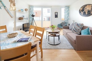 Een woonkamer met een bank, een eettafel met stoelen, een televisie en een klein rond tafeltje met een plant.