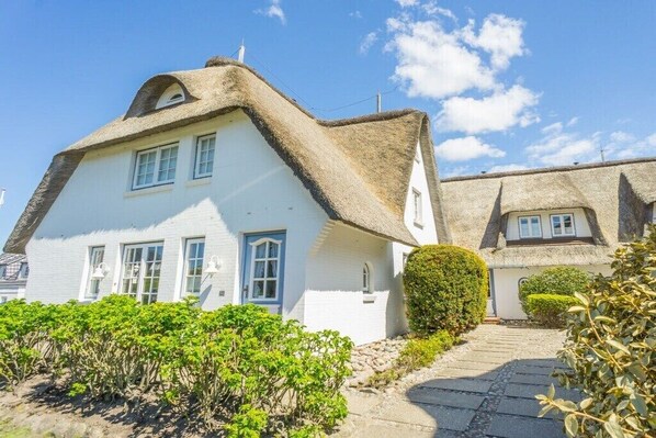 A white house with a thatched roof, a stone pathway, and a hedge in front. - Apartment in Rantum with swimming pool (Rantum)