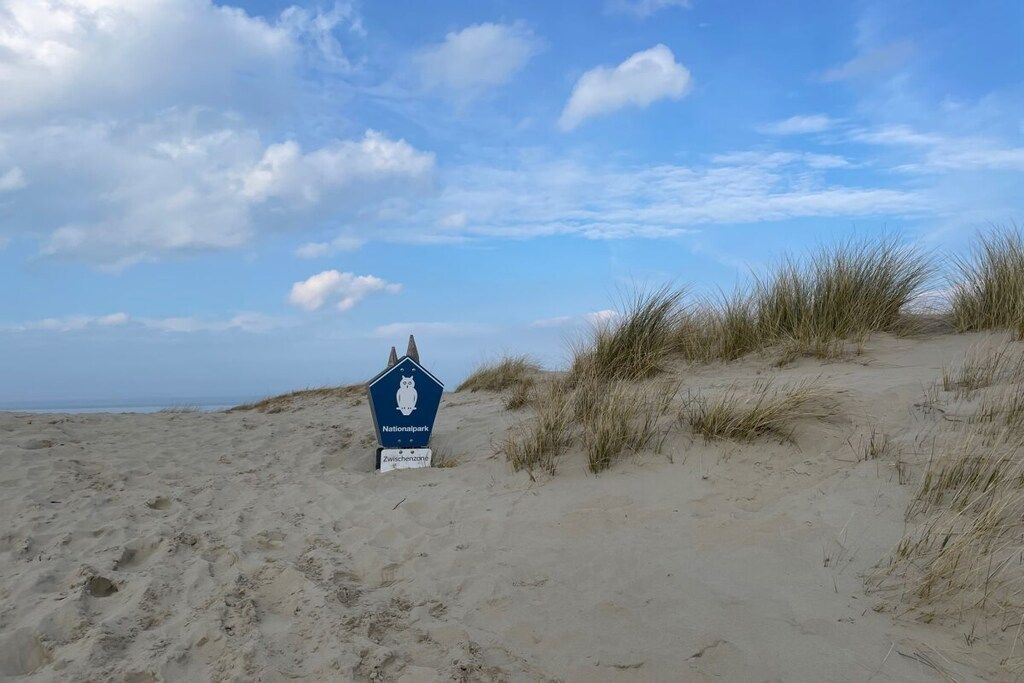 Señal de un parque nacional en una playa arenosa con dunas y cielo despejado.