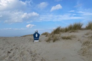 Schild für einen Nationalpark an einem sandigen Strand mit Dünen und blauem Himmel.