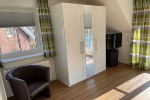 Ein Zimmer mit großem Kleiderschrank, Fernseher, Stuhl und einem fenster mit Vorhängen.