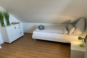 Ein modernes Schlafzimmer mit einem weißen Bett, einem Nachttisch, einer Lampe und einem kleinen Tisch mit einer Pflanze.