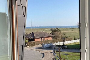 Vista desde una ventana que da a un paisaje rural con una casa, una valla y cielo despejado.