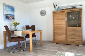 A dining area with a wooden table and chairs, a clock on the wall, and a cabinet with glass doors. - Holiday apartment with 1 bedroom (Maasholm)