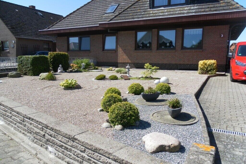A residential property with a gravel driveway, potted plants, and a red car parked in the driveway.