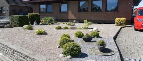 A residential property with a gravel driveway, potted plants, and a red car parked in the driveway.