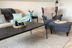 A modern living room with a sofa, armchair, coffee table, and decorative items. - Holiday apartment with 1 bedroom (Maasholm)
