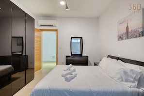 A hotel room with a bed, a desk, a mirror, and a wall-mounted air conditioner. - Bright Sliema 1-BR | Balcony | Lift | Near Ferries (Sliema)