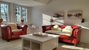 A living room with two red leather sofas, a white coffee table, and a window with a view of trees. - Holiday apartment in Ratekau with barbecue (Ratekau)