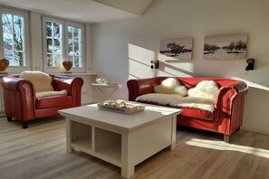 A living room with two red leather sofas, a white coffee table, and a window with a view of trees. - Holiday apartment in Ratekau with barbecue (Ratekau)