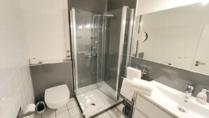 A modern bathroom with a glass-enclosed shower, a toilet, and a sink with a mirror. - Holiday apartment in Ratekau with barbecue (Ratekau)