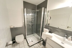A modern bathroom with a glass-enclosed shower, a toilet, and a sink with a mirror. - Holiday apartment in Ratekau with barbecue (Ratekau)