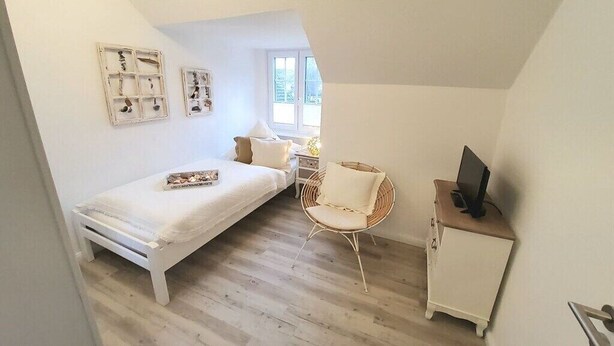 A bedroom with a bed, a chair, a desk with a computer, and a window. - Holiday apartment in Ratekau with barbecue (Ratekau)