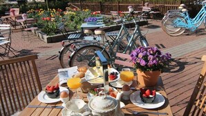 An outdoor breakfast setting with a wooden table, breakfast items, a bicycle, and a flower pot. - Holiday apartment in Ratekau with barbecue (Ratekau)