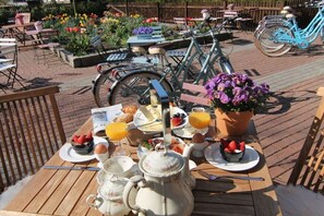 An outdoor breakfast setting with a wooden table, breakfast items, a bicycle, and a flower pot. - Holiday apartment in Ratekau with barbecue (Ratekau)