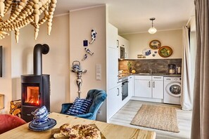 A cozy living room with a wood-burning stove, a dining area with a table set for two, and a kitchen with modern appliances. - Holiday apartment in Büsum with swimming pool (Büsum)