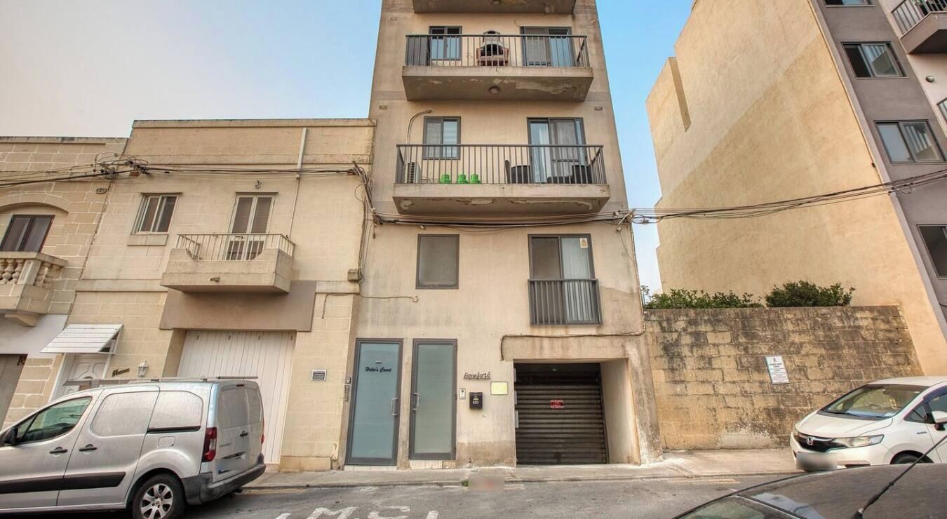 A multi-story building with a ground-level entrance, a balcony on the second floor, and a garage door on the ground floor.
