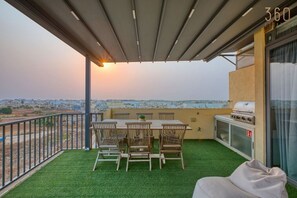 Ein Balkon mit Tisch und Stühlen, einem Grill und Blick auf die Stadtlandschaft.