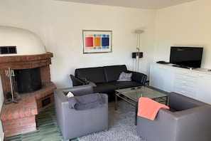 Un saló amb una llar de pedra, un sofà de cuir negre, una taula de centre de vidre i una televisió de pantalla plana sobre un moble.