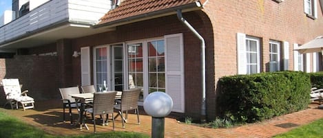 A brick house with a covered patio, outdoor furniture, and a hedge.