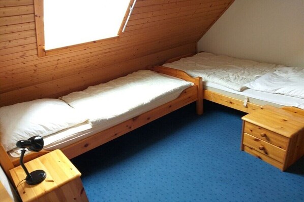 Ein kleines Zimmer mit einem Einzelbett, geneigter Decke, Holzwänden und blauem Teppich.