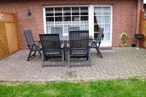 Eine Terrasse mit Tisch und Stühlen, ein hölzernes Tor und ein Fenster mit Vorhängen.