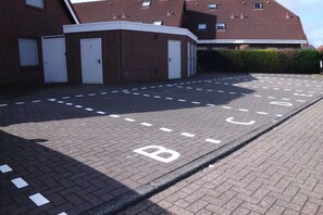 Ein Parkplatz mit ausgewiesenen Fahrradstellplätzen und einem Gebäude mit Backsteinmauern und roten Ziegeldächern.