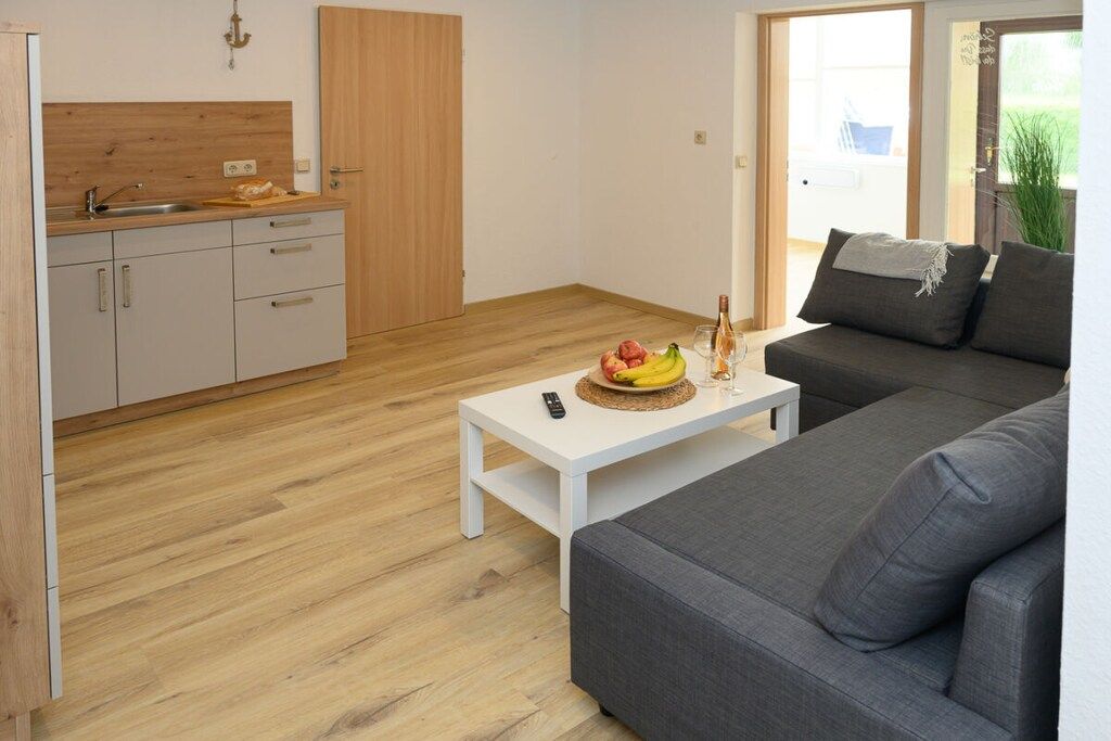 A modern living space with a kitchen, a white coffee table with fruits, and a grey sofa.
