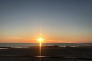 A beach scene with the sun setting over the horizon, a clear sky, and a calm sea. - Holiday apartment with 1 bedroom (Aurich)