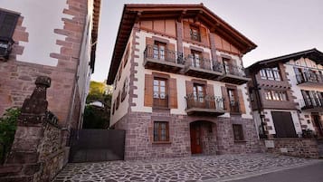 Un edifici de diverses plantes amb balcons, façana de pedra i carrer empedrat.