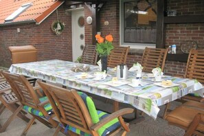 Un área de comedor al aire libre con una mesa cubierta por un mantel estampado, rodeada de sillas de madera con cojines.
